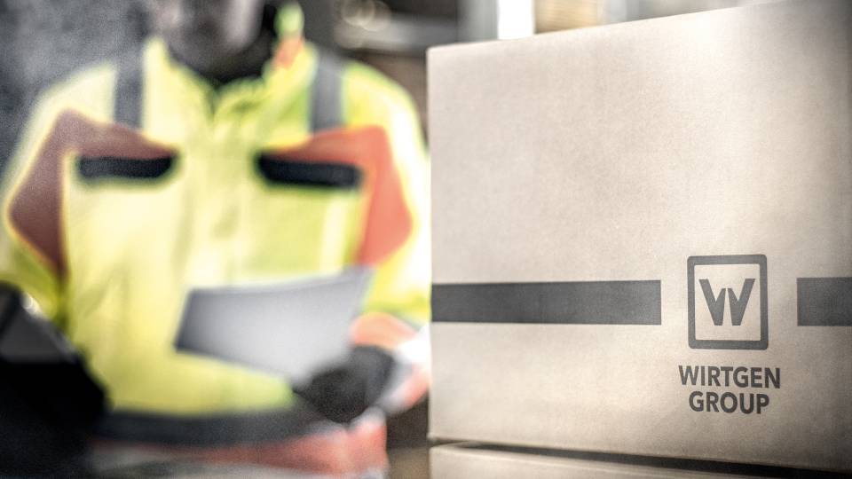 Paket zum Versand von Ersatzteilen mit Mitarbeiter im Hintergrund Paket zum Versand von Ersatzteilen mit Mitarbeiter im Hintergrund